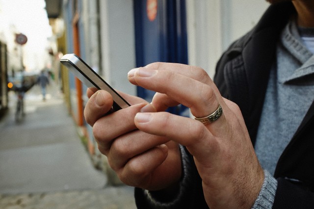 Mid adult man on sidewalk using touchscreen on smartphone